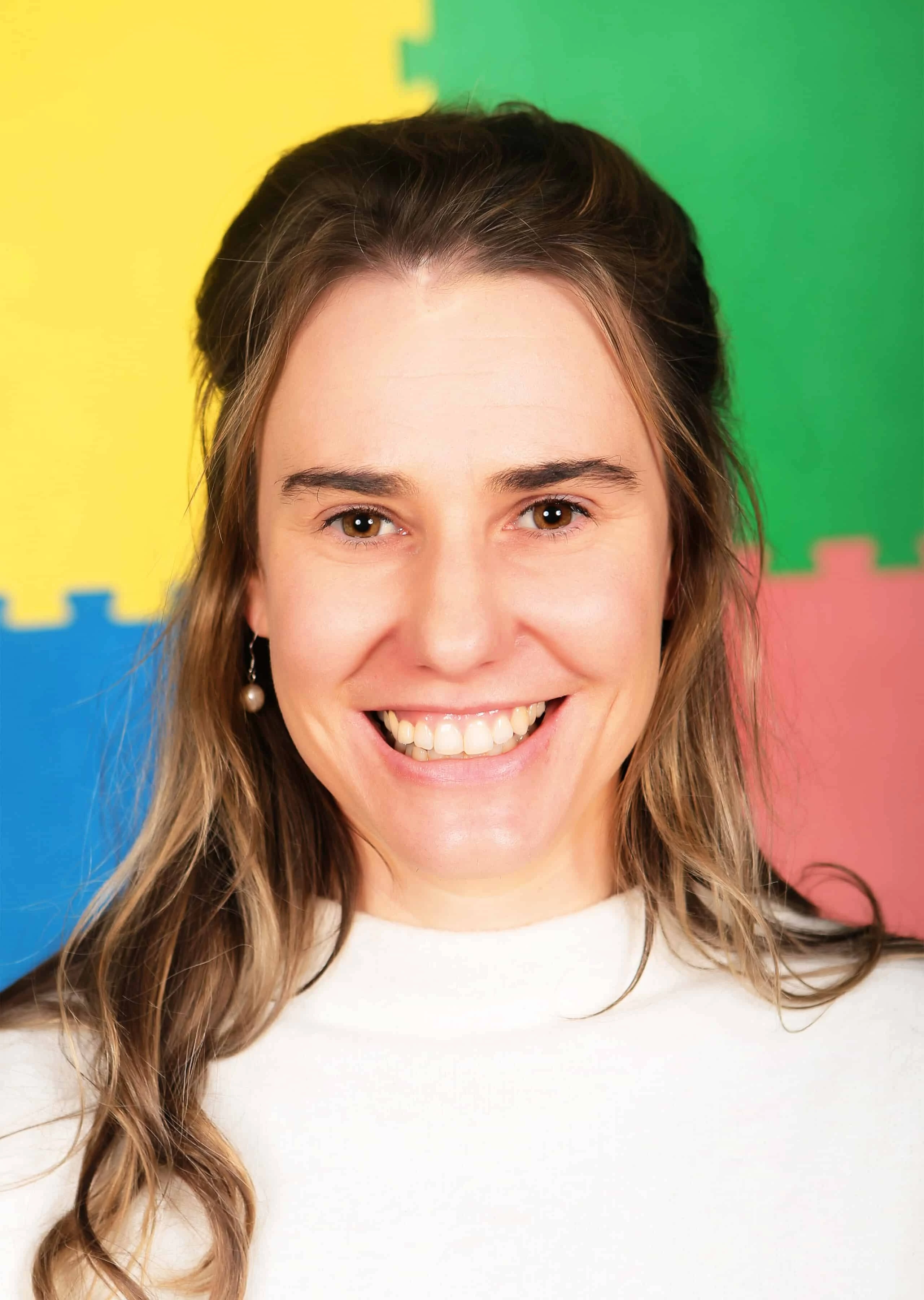 Samantha Smiling Samantha with long hair, standing against a colorful foam mat background