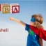 Child dressed as a superhero with a cape, posing with blocks spelling 'ABA' to represent Applied Behavior Analysis