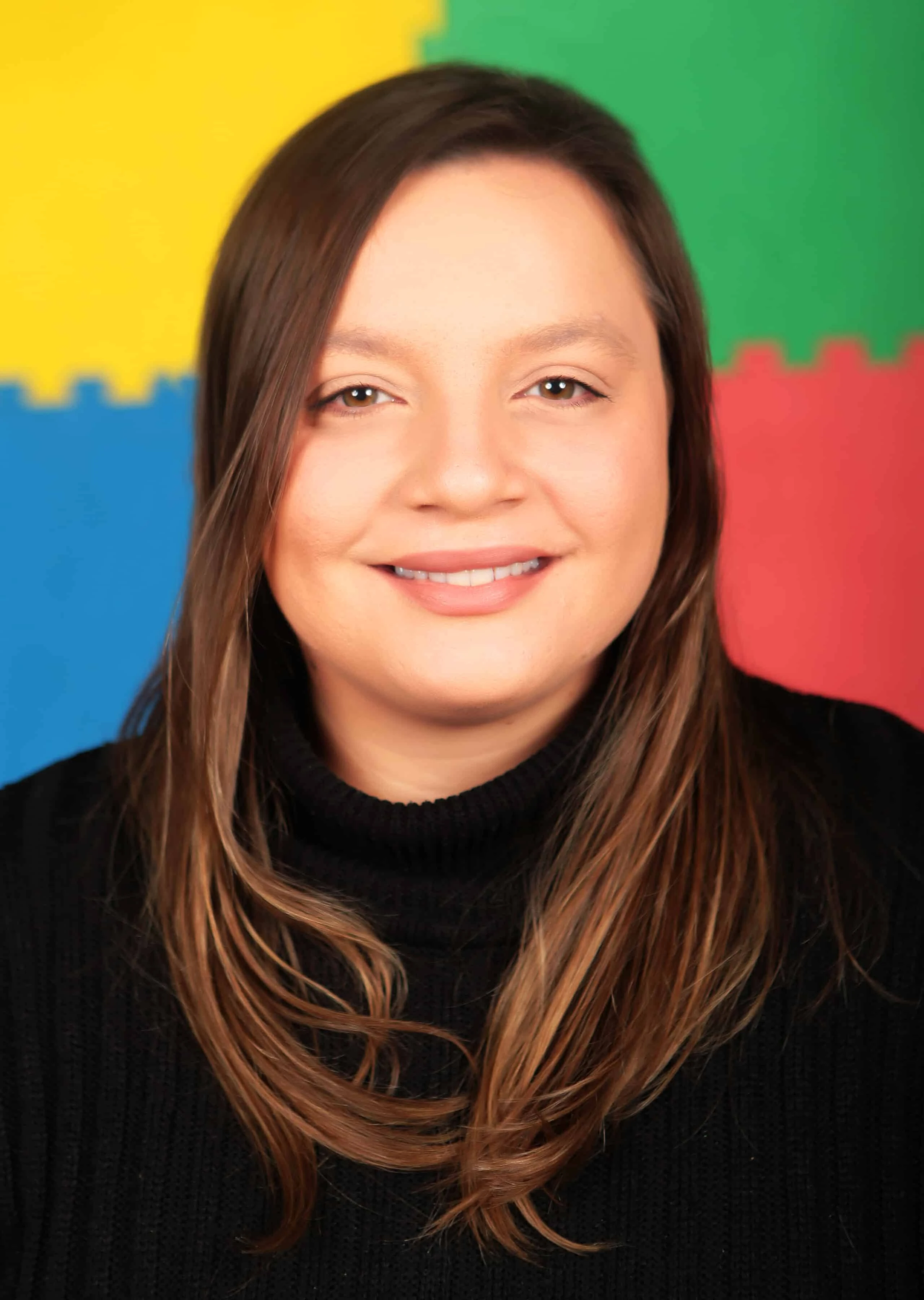 Giulia Portrait of Giulia with brown hair, wearing a black sweater, and smiling against a colorful background of foam mats